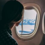 A woman looks out an airplane window, capturing a serene view of clouds and sky during a flight.