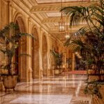 Luxurious hotel lobby featuring elegant lighting and marble flooring, accented by lush indoor plants.