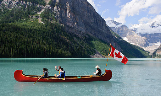 Men canoeing in St Louise Lake, Banff National Park with a Canadian Flag, one waving