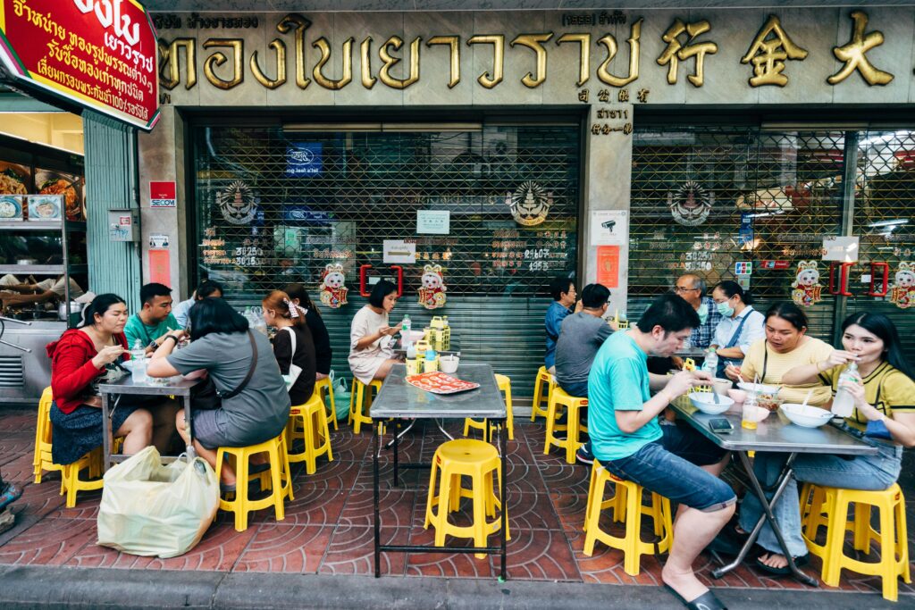 People enjoying authentic Thai street food at outdoor tables in Bangkok city.