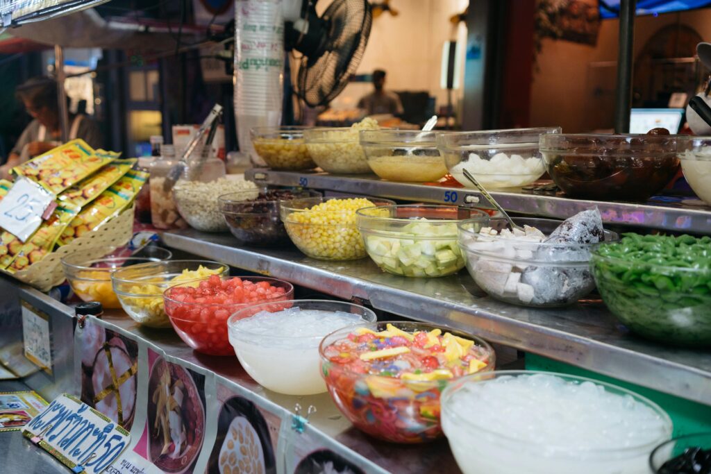Colorful array of Thai desserts and ingredients at a bustling market stall, showcasing authentic culinary culture.