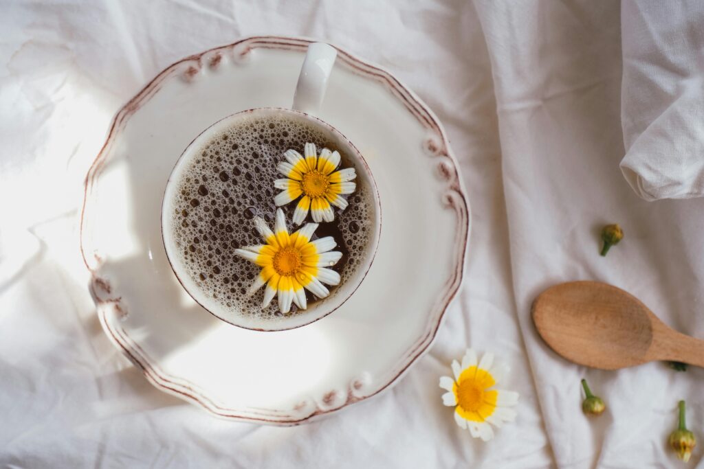 A rustic cup of herbal tea with daisies on a white bedspread for a cozy morning vibe.