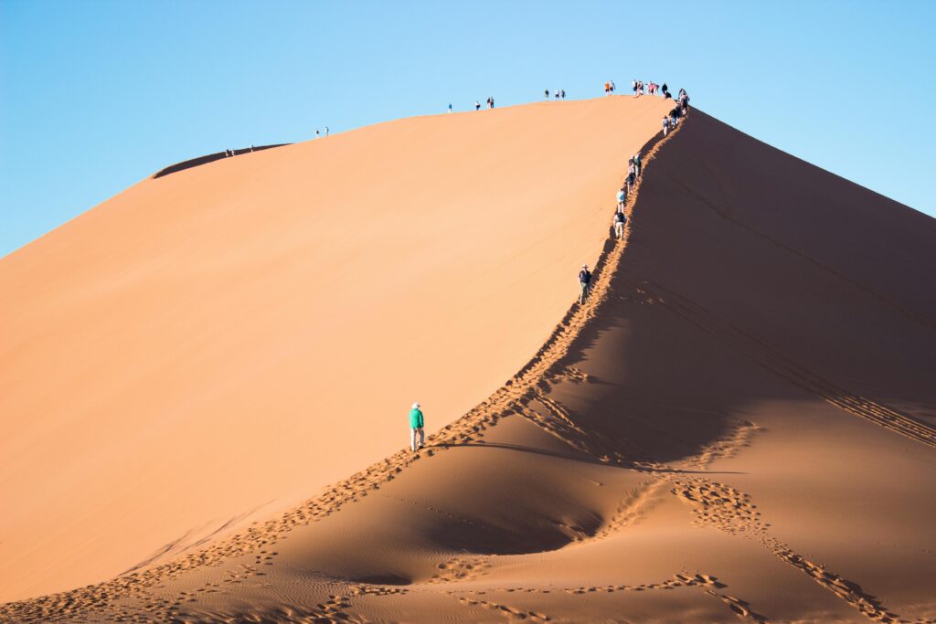 Tourists trek up a vast sand dune under the clear blue skies of Namibia's desert landscape.